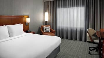 A hotel room with a large bed, a nightstand with a lamp, a chair, and a desk.