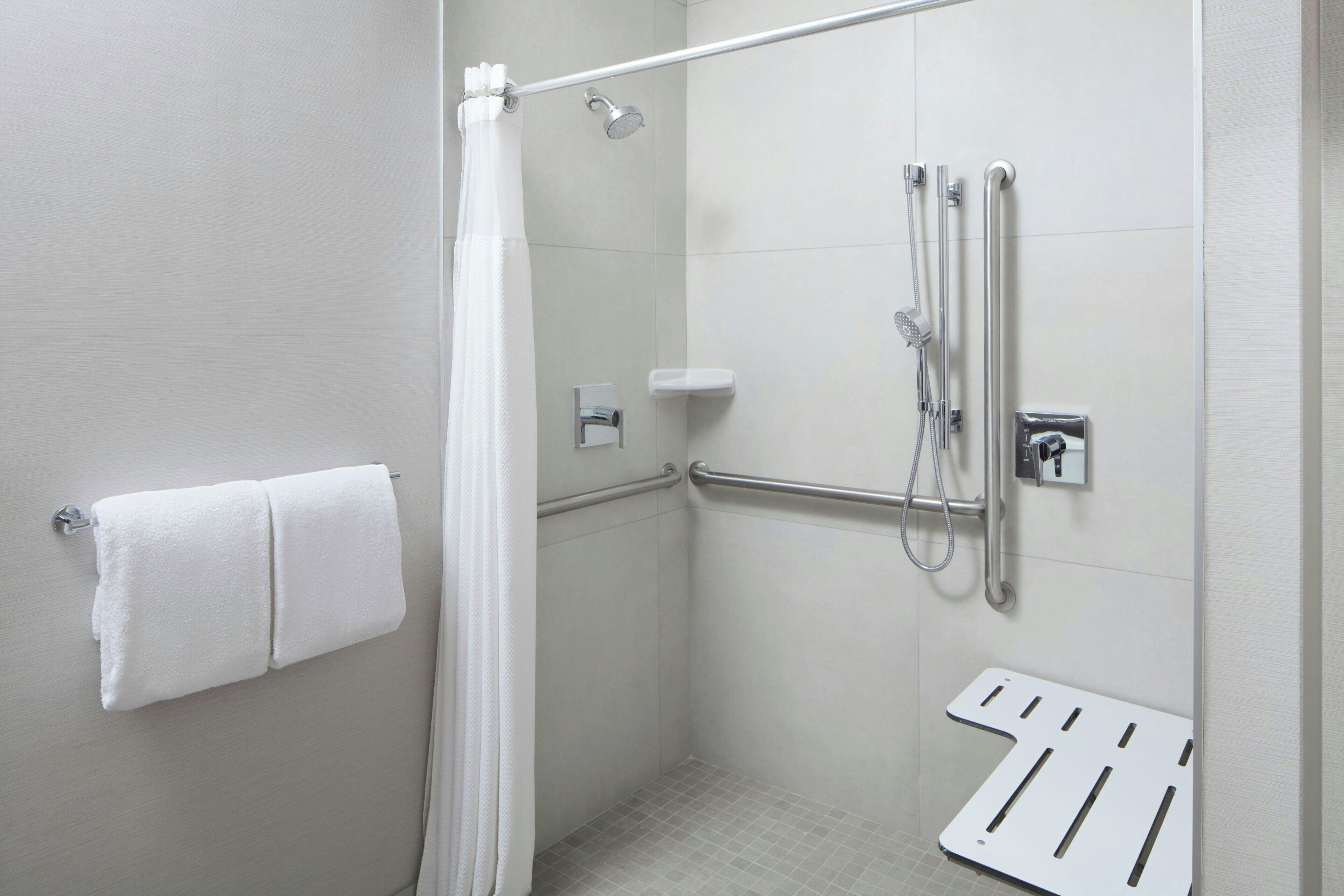 A modern shower area with a grab bar, a towel rack, and a showerhead.