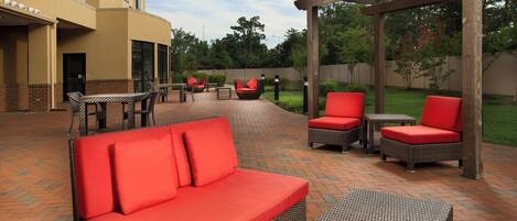 An outdoor patio area with wicker furniture, red cushions, and a pergola structure.