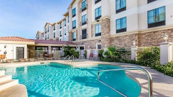 A swimming pool with steps leading into it, surrounded by a building with multiple balconies and a covered patio area.