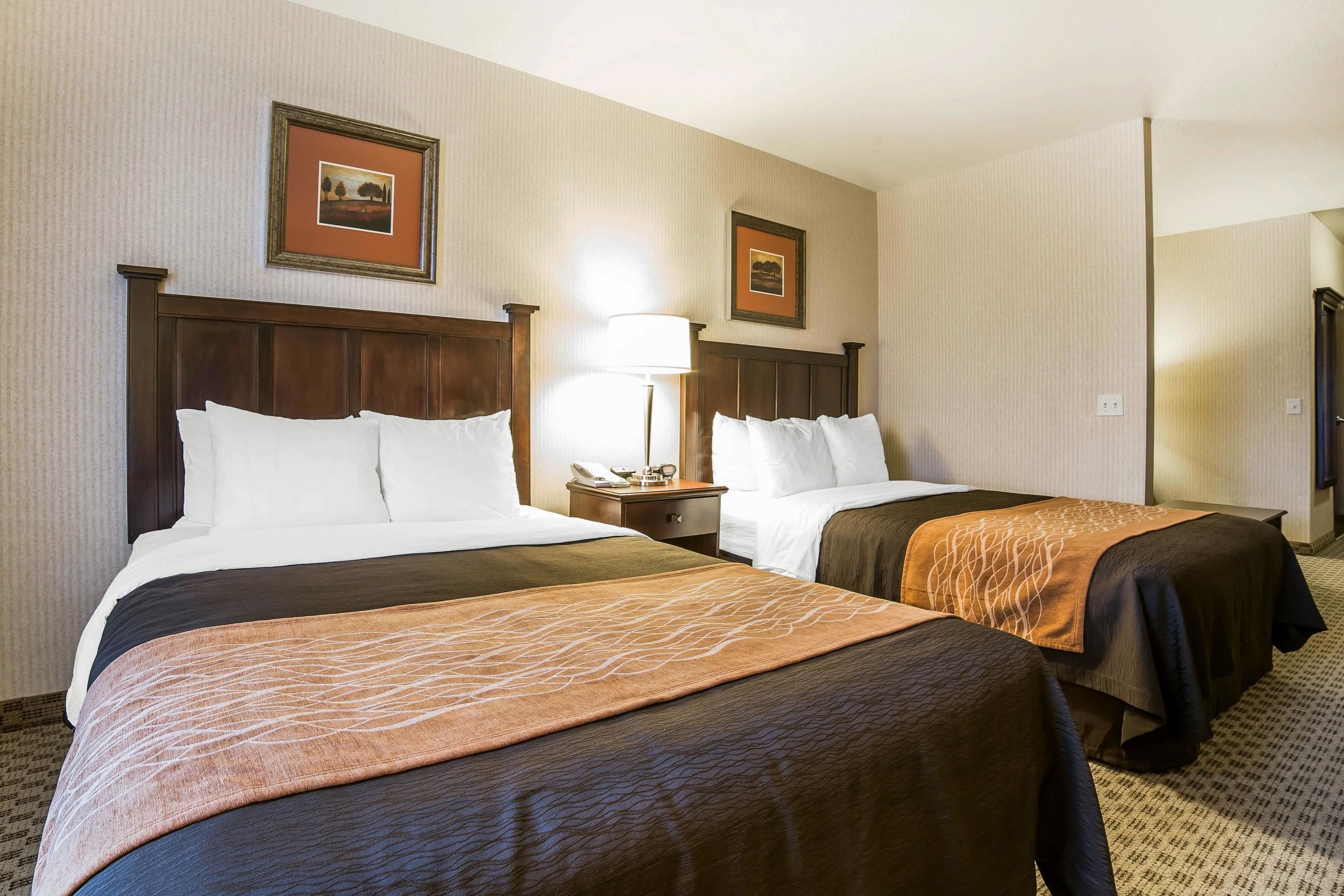 A hotel room with two beds, each with a wooden headboard, a nightstand with a lamp, and framed pictures on the wall.