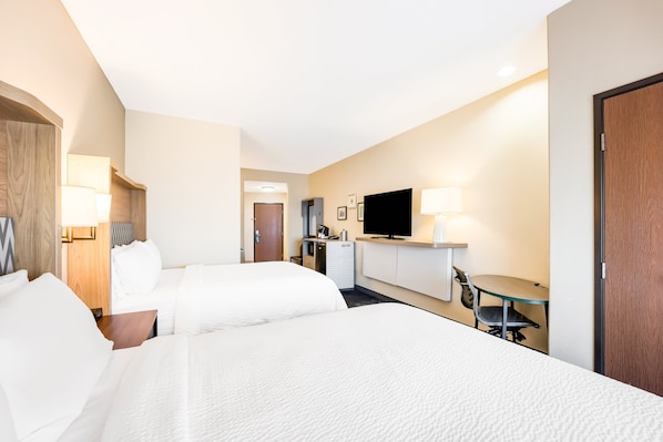 A hotel room with two beds, a desk, a television, and a minibar.