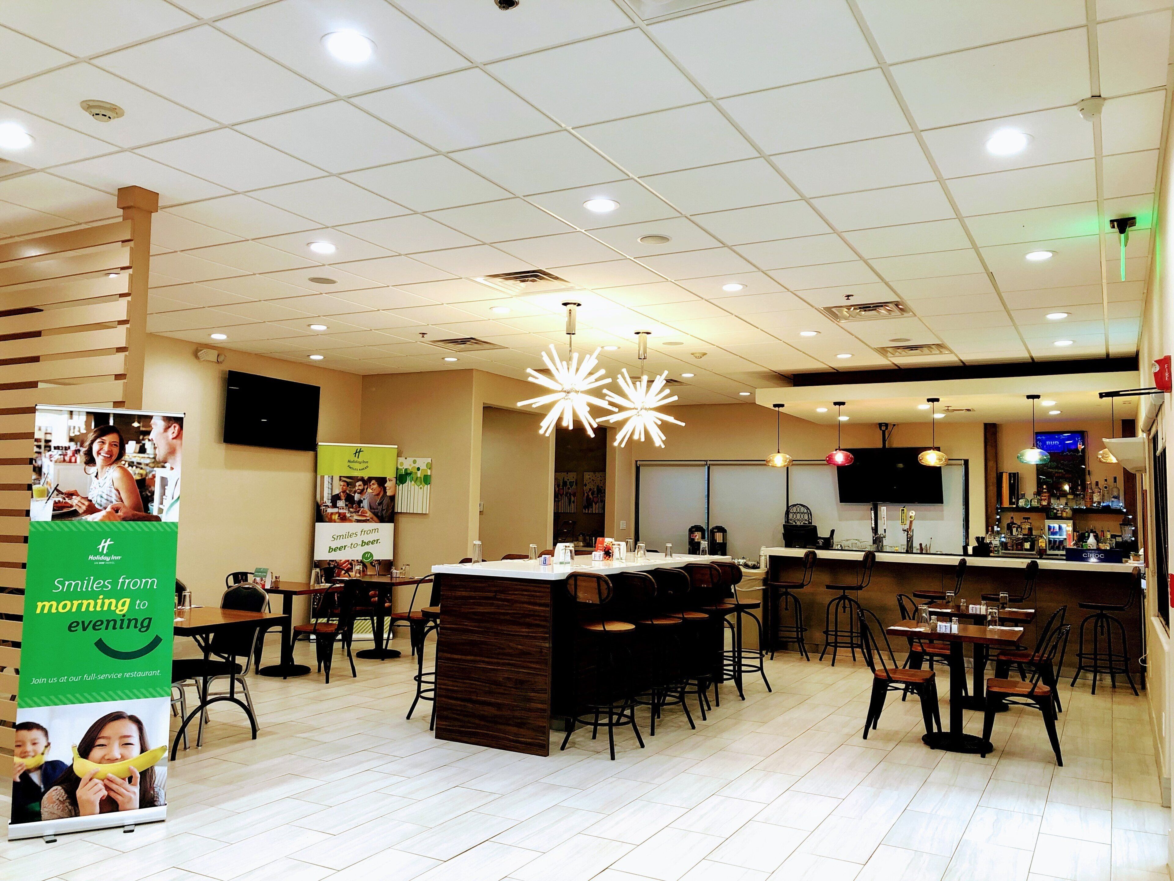 A restaurant with a bar area, multiple tables, and a large illuminated ceiling fixture.