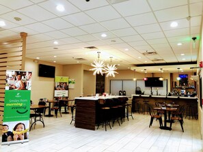 A restaurant with a bar area, multiple tables, and a large illuminated ceiling fixture. - Holiday Inn Brownsville by IHG (Brownsville)