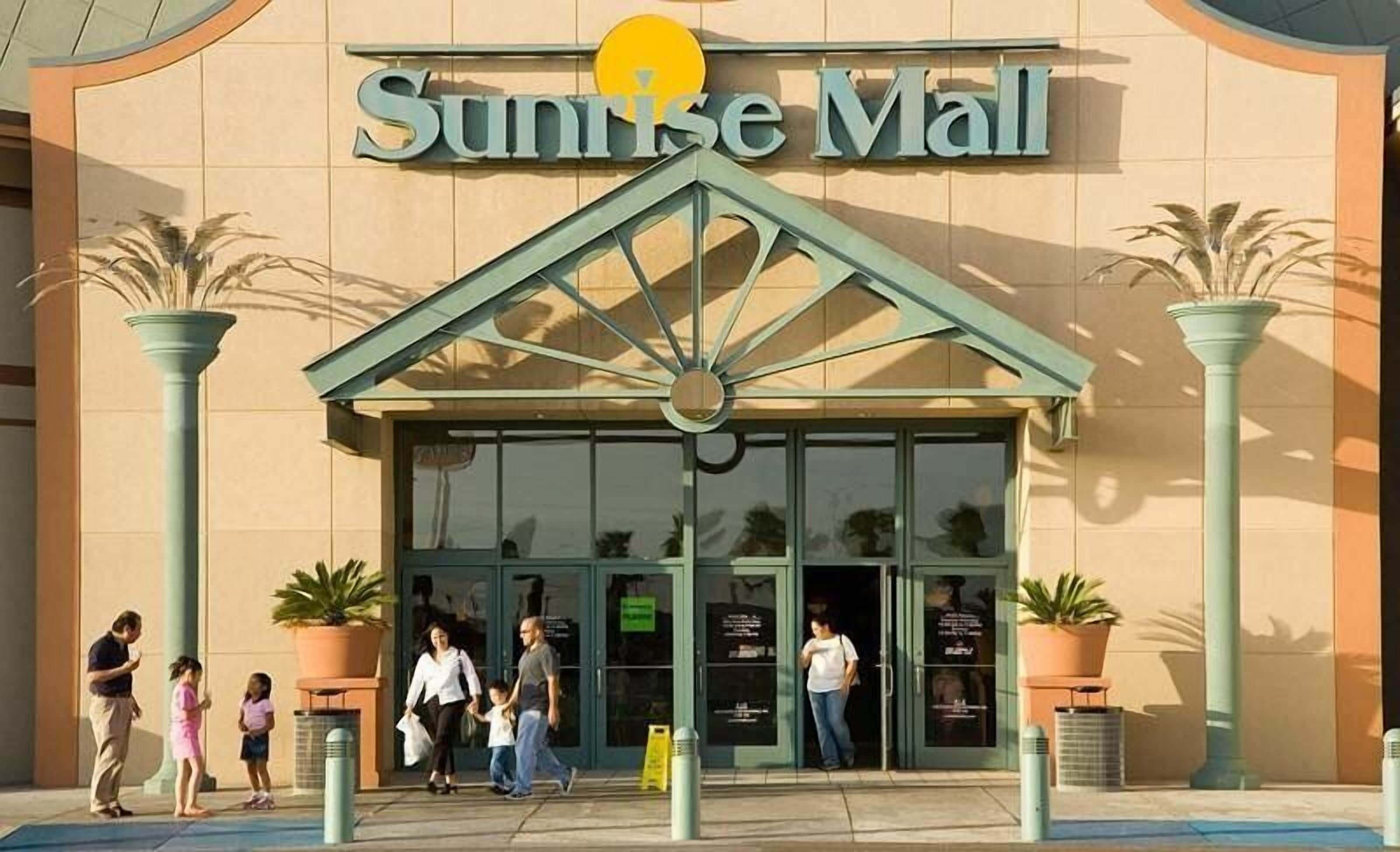 The exterior of Sunrise Mall with a central entrance, potted plants, and a clear sky.