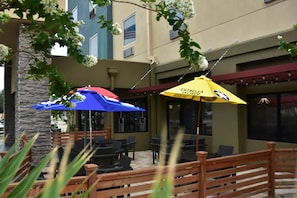 An outdoor seating area with wooden benches and tables, covered by blue and yellow umbrellas, and a stone pillar. - Holiday Inn Brownsville by IHG (Brownsville)