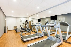 Un gimnasio con cintas de correr, bicicletas estáticas y un espejo grande.