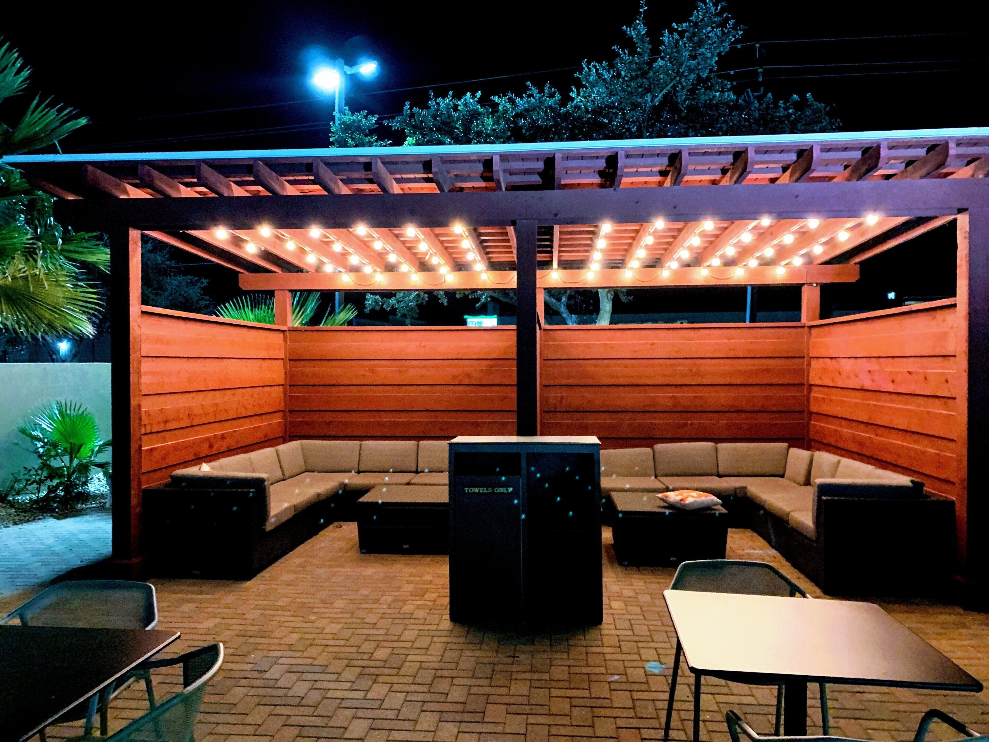 An outdoor patio area with a wooden pergola, cushioned seating, and a table.