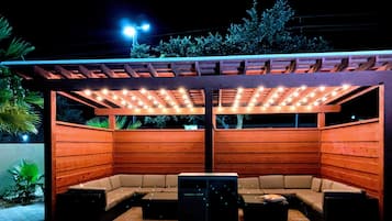 An outdoor patio area with a wooden pergola, cushioned seating, and a table.