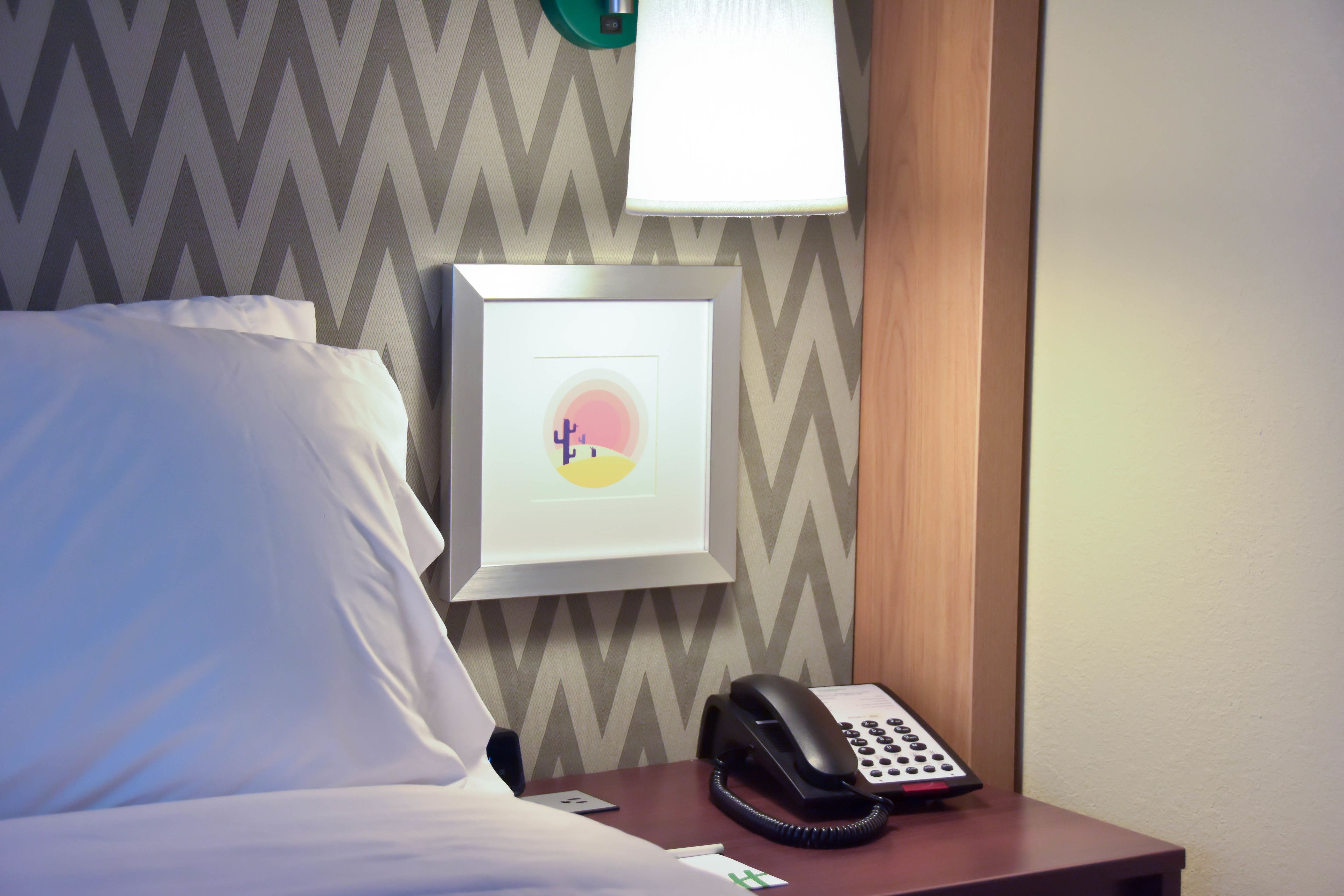 Habitación de hotel con cama, mesita de noche con teléfono, cuadro enmarco y pared con diseño en zigzag.