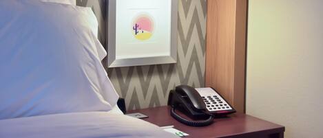 Habitación de hotel con cama, mesita de noche con teléfono, cuadro enmarco y pared con diseño en zigzag.
