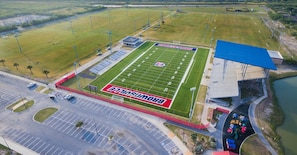 An aerial view of a football stadium with a large field, stadium seating, and a parking area.