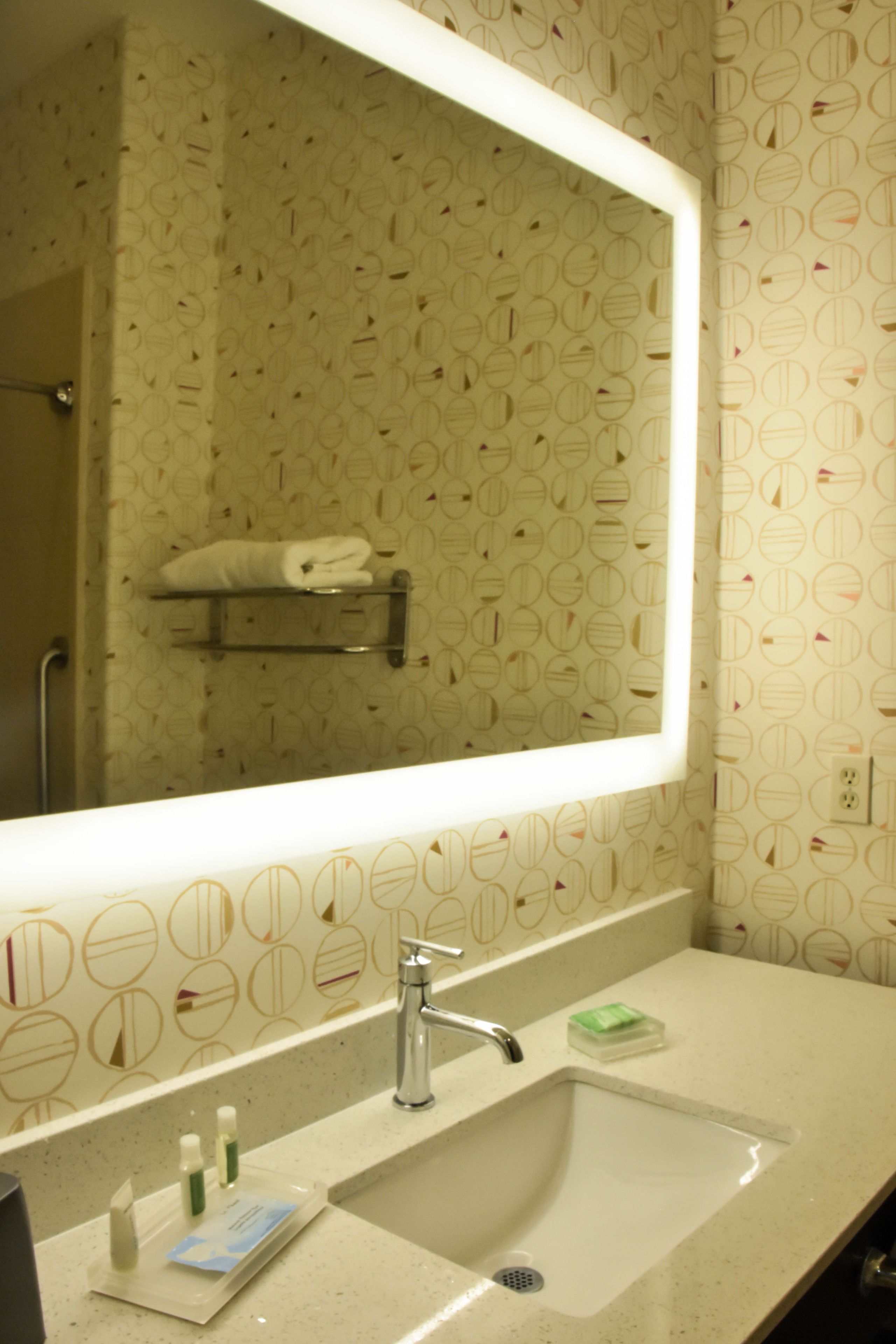 Une salle de bain avec un grand miroir, un lavabo et un porte-serviettes.