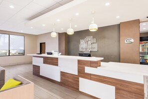 A hotel reception area with a modern design, featuring a reception desk, a wall-mounted sign, and a vending machine.