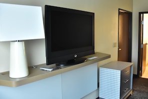 A hotel room with a flat-screen TV on a stand, a white lamp, and a patterned storage unit.