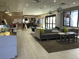 Un interior moderno con una zona de estar, una barra con exhibición de alimentos y ventanas amplias.