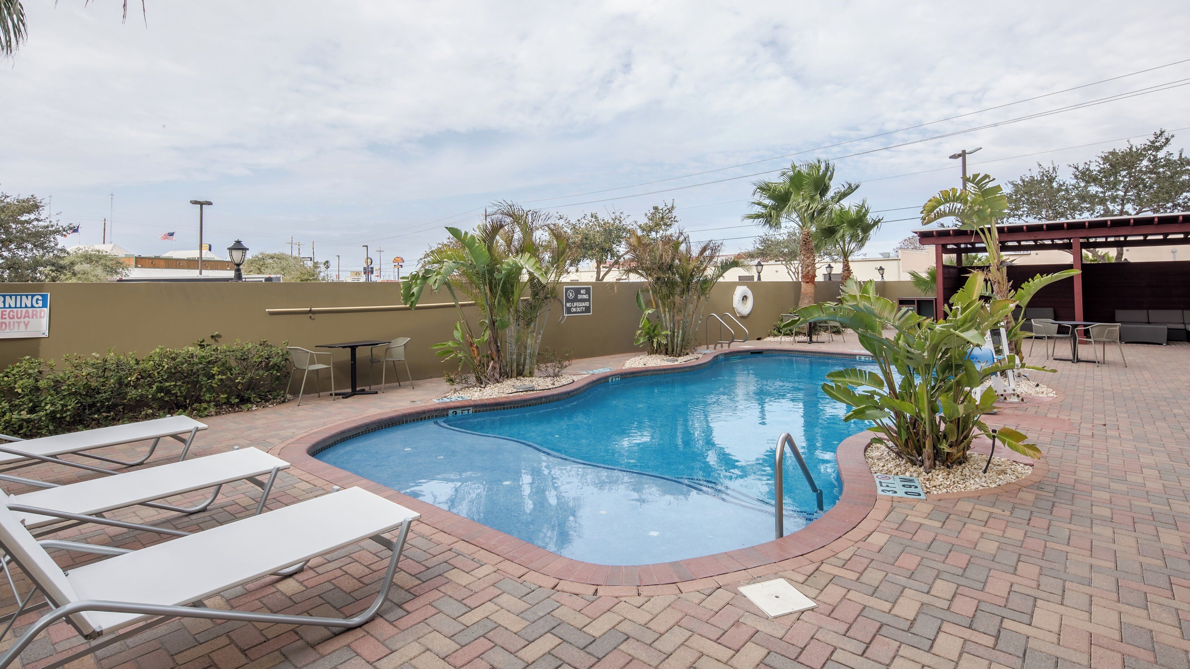 A swimming pool with a brick patio, lounge chairs, and a lifeguard duty sign.