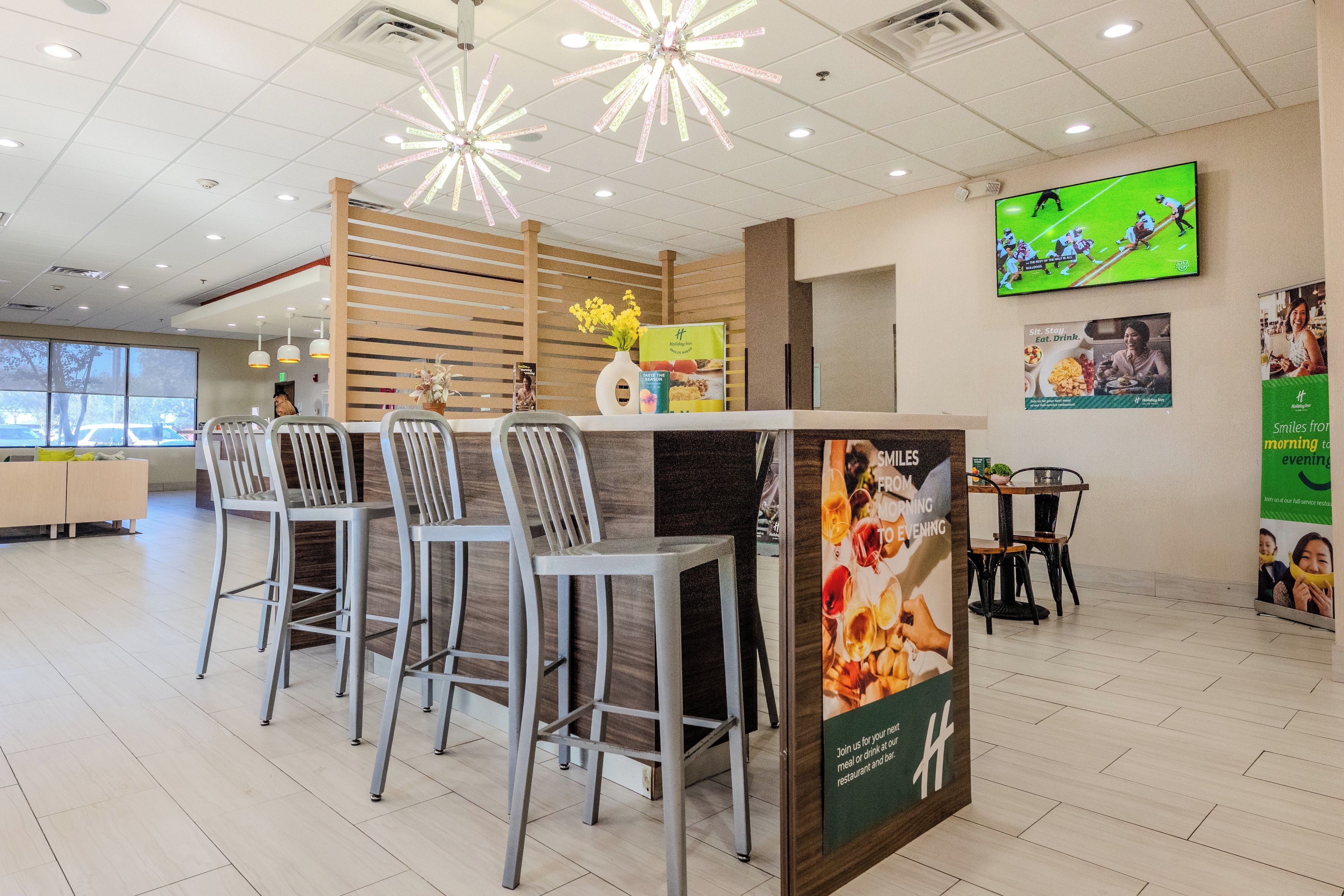 A modern restaurant interior with a bar area, seating, and a large screen displaying a sports event.