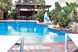 A swimming pool with a diving board, surrounded by plants and outdoor seating. - Holiday Inn Brownsville by IHG (Brownsville)