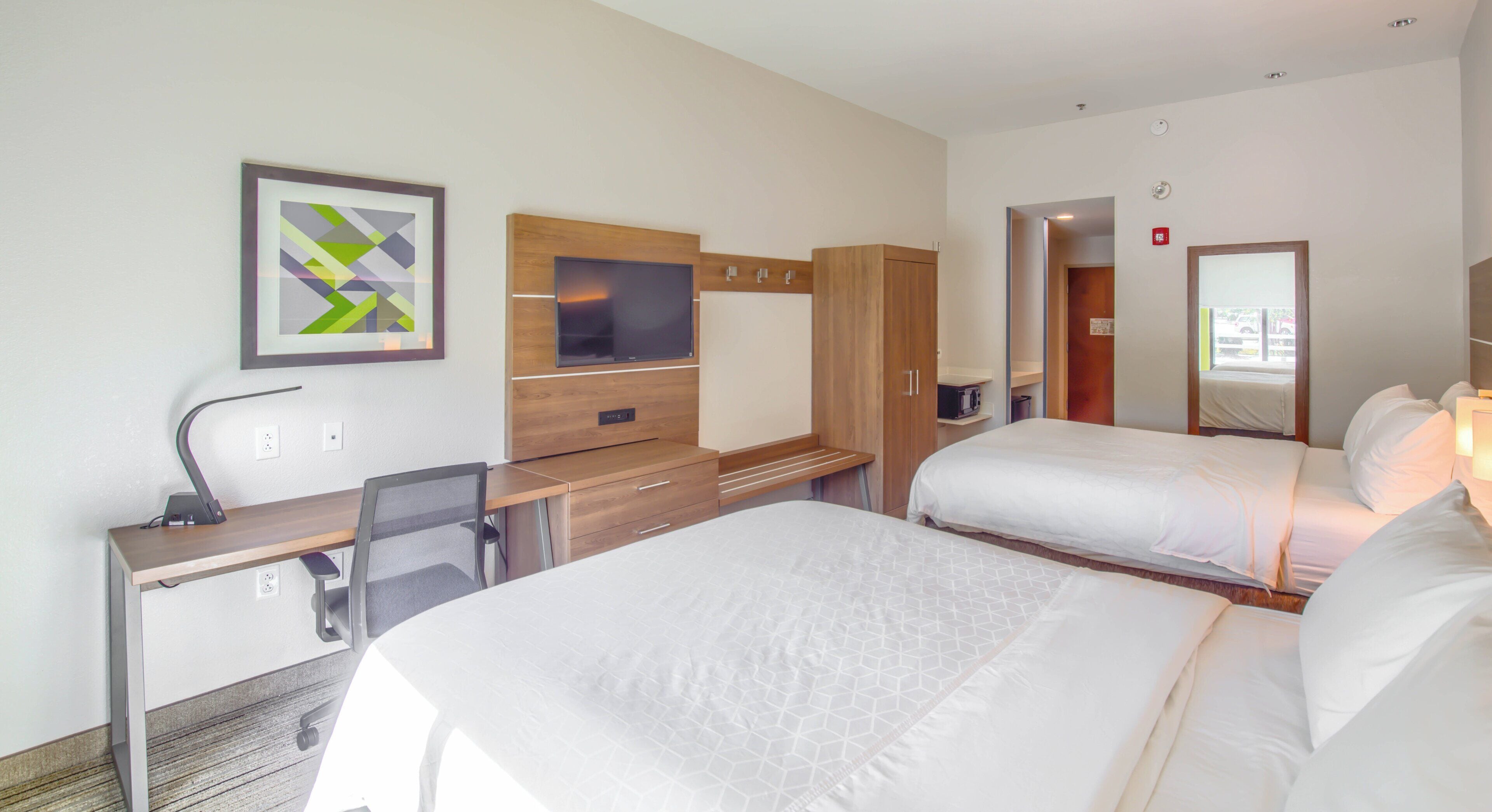 Una habitación de hotel con una cama, un escritorio con silla, un televisor y un armario.