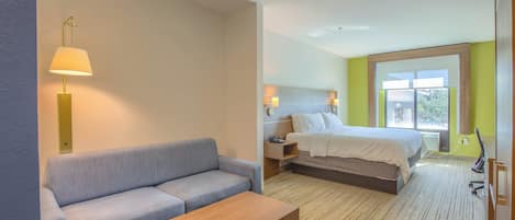 A hotel room with a sofa, a wooden table, a bed, bedside lamps, and a window with a view.