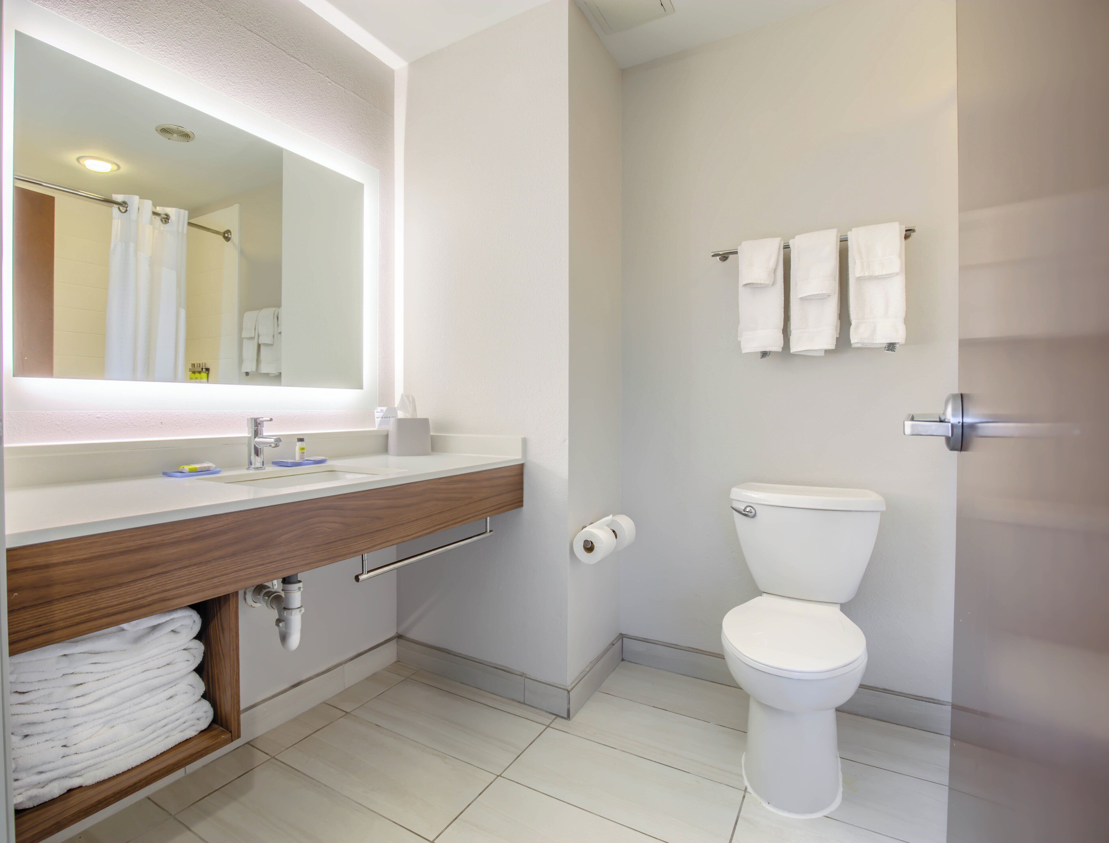 A modern bathroom with a white toilet, a sink with a wooden vanity, a mirror, and a towel rack.