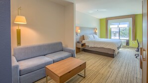A hotel room with a sofa, a wooden table, a bed, a nightstand, and a window with a view. - Holiday Inn Express & Suites Gulf Shores by IHG (Gulf Shores)