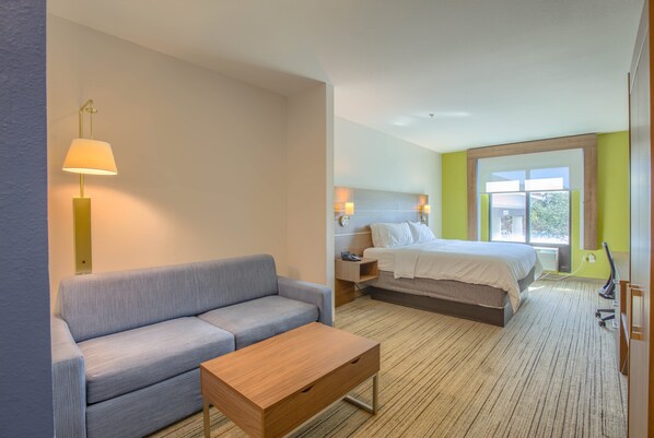A hotel room with a sofa, a wooden table, a bed, a nightstand, and a window with a view. - Holiday Inn Express & Suites Gulf Shores by IHG (Gulf Shores)