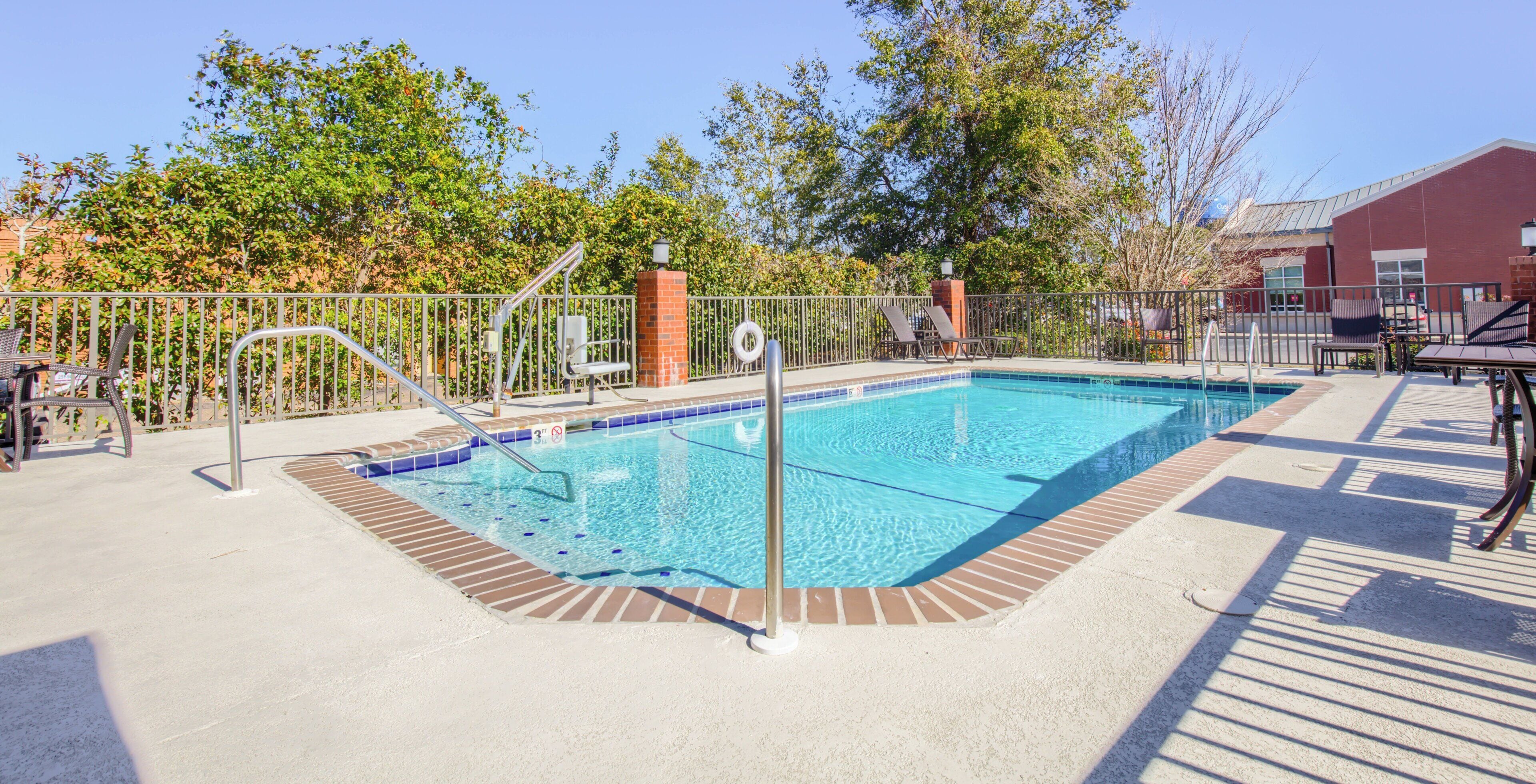 Ein rechteckiger Swimmingpool mit einer gefliesten Kante, umgeben von einem Metallzaun und mit einer Leiter ausgestattet.