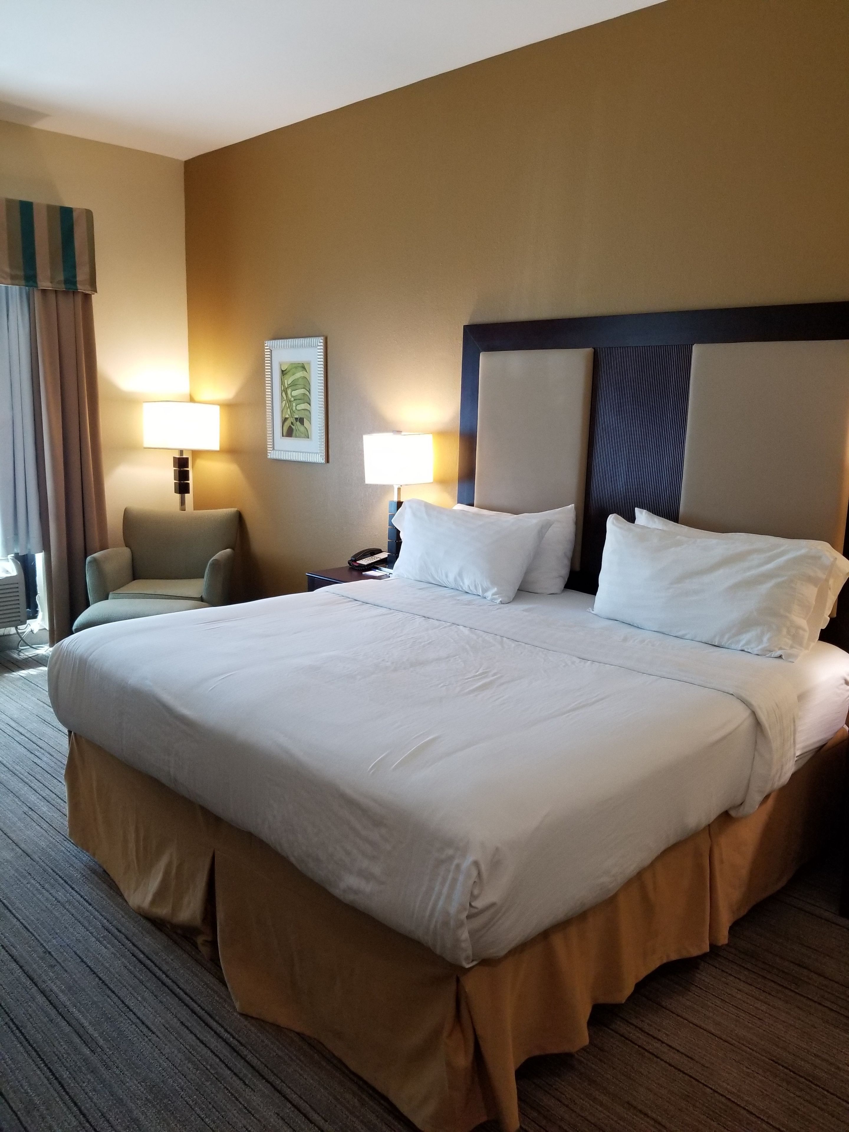 A hotel room with a large bed, two bedside tables, a chair, and a window with curtains.