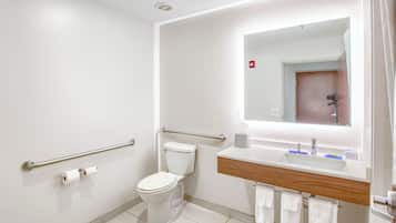 A modern bathroom with a toilet, handrails, a sink with a mirror, and a towel rack.