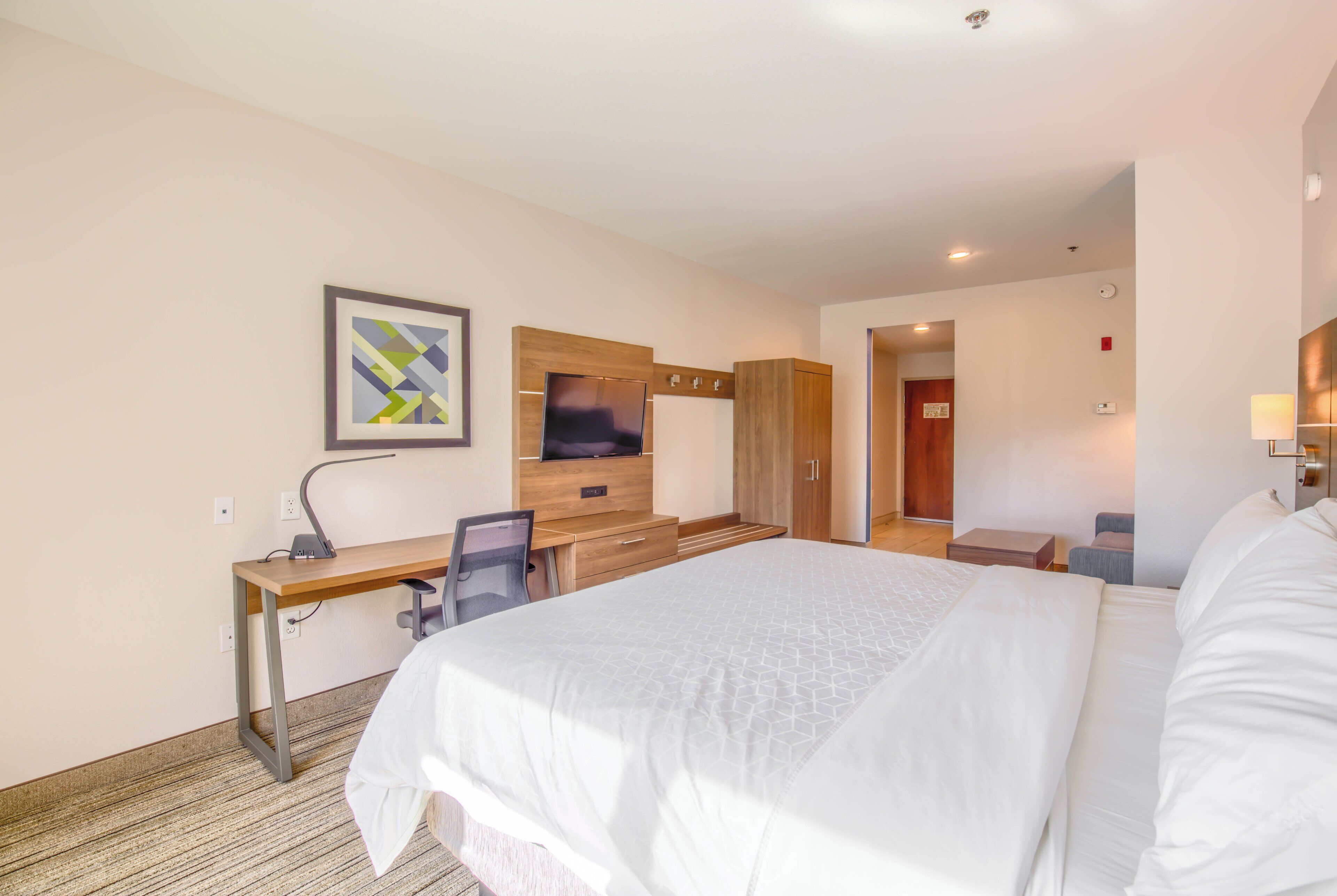 A hotel room with a large bed, a desk with a chair, a television, and a wardrobe.