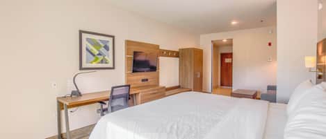 Una habitación de hotel con una cama grande, un escritorio con una silla, un televisor y un armario.