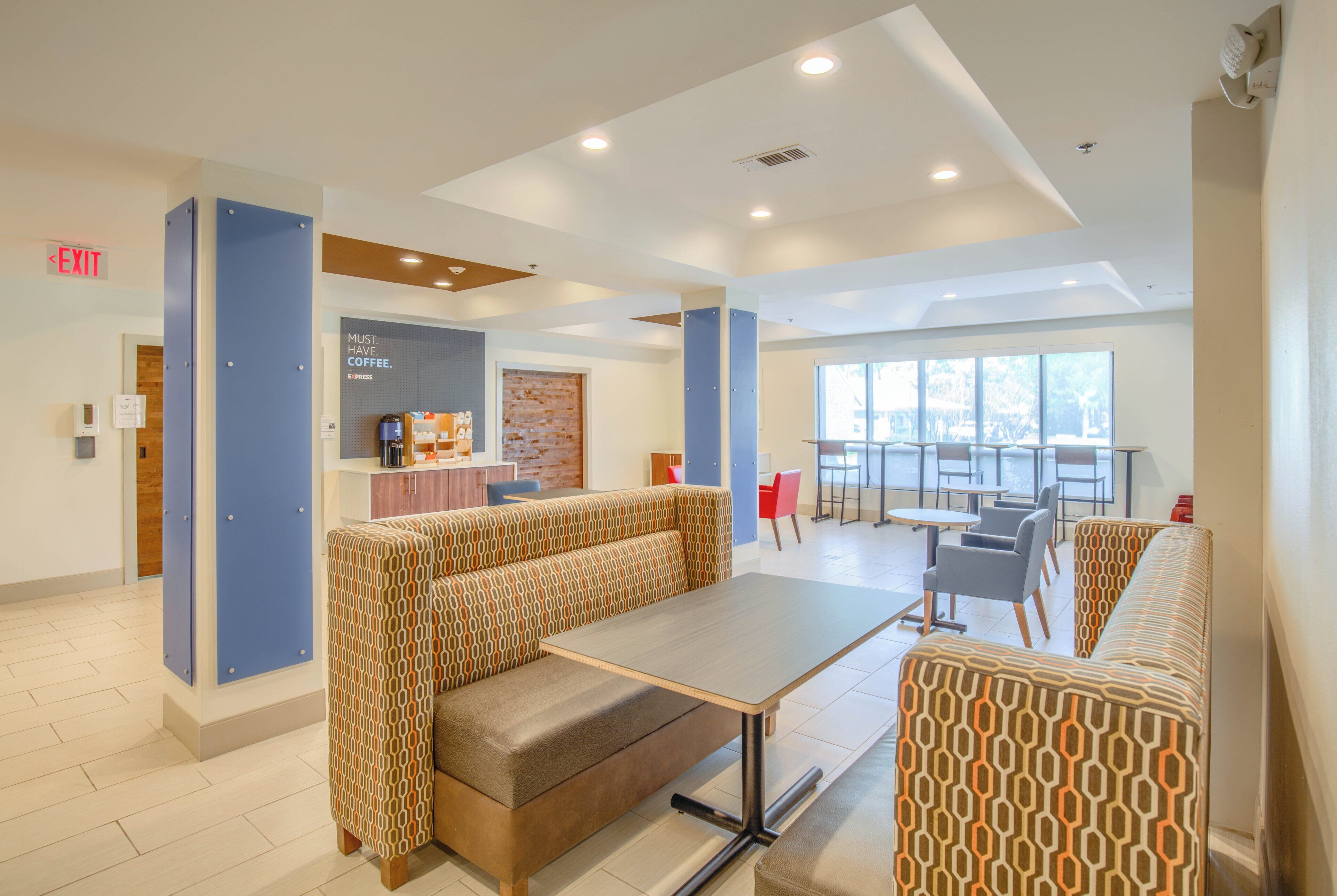 A modern interior with seating areas, a coffee station, and a view through large windows.