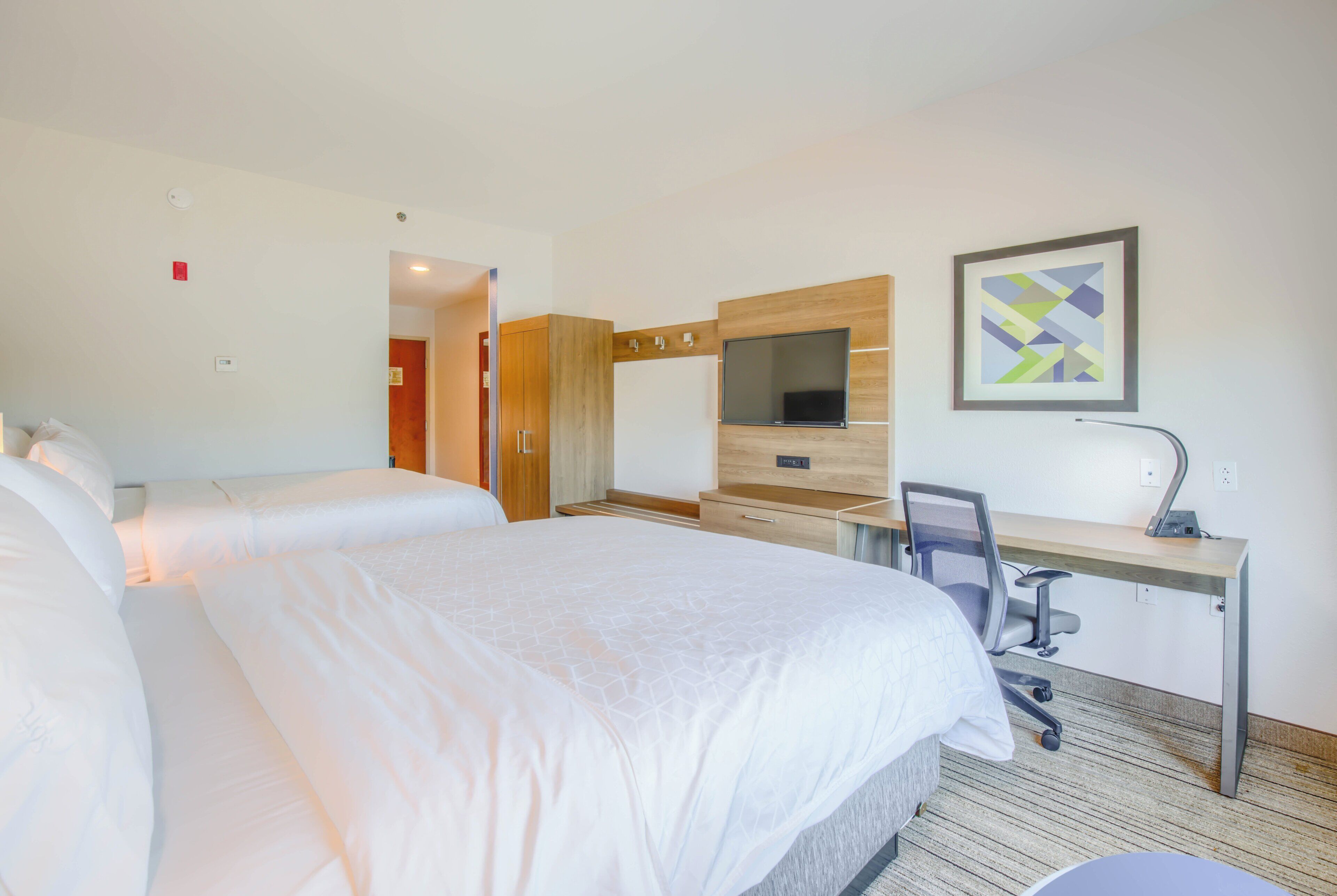 Habitación de hotel con dos camas, un escritorio con silla, televisión y un cuadro abstracto enmarcado.