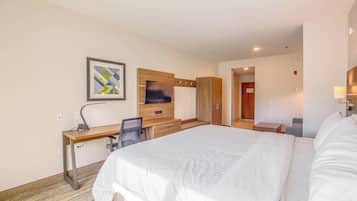 Une chambre d’hôtel avec un grand lit, un bureau avec une chaise, une télévision et une armoire.