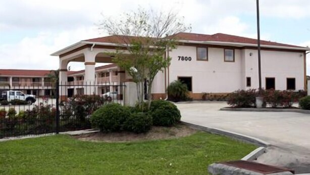 A two-story building with a flat roof, numbered 7800, surrounded by a fence and greenery. - Express Inn and Suites (Westwego)