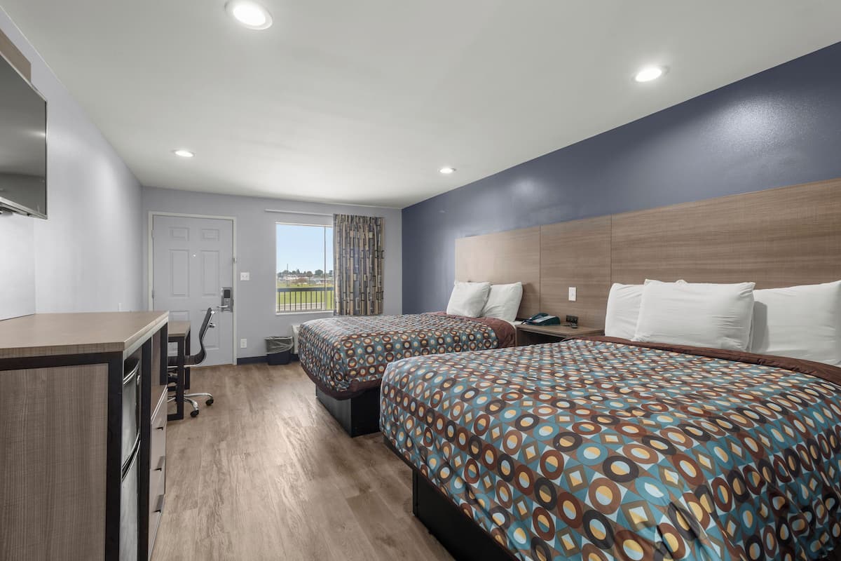 Quarto de hotel com duas camas, uma escrivaninha e vista para o exterior.