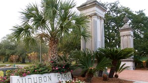 A sign for Audubon Park with a garden of flowers and palm trees. - Express Inn and Suites (Westwego)