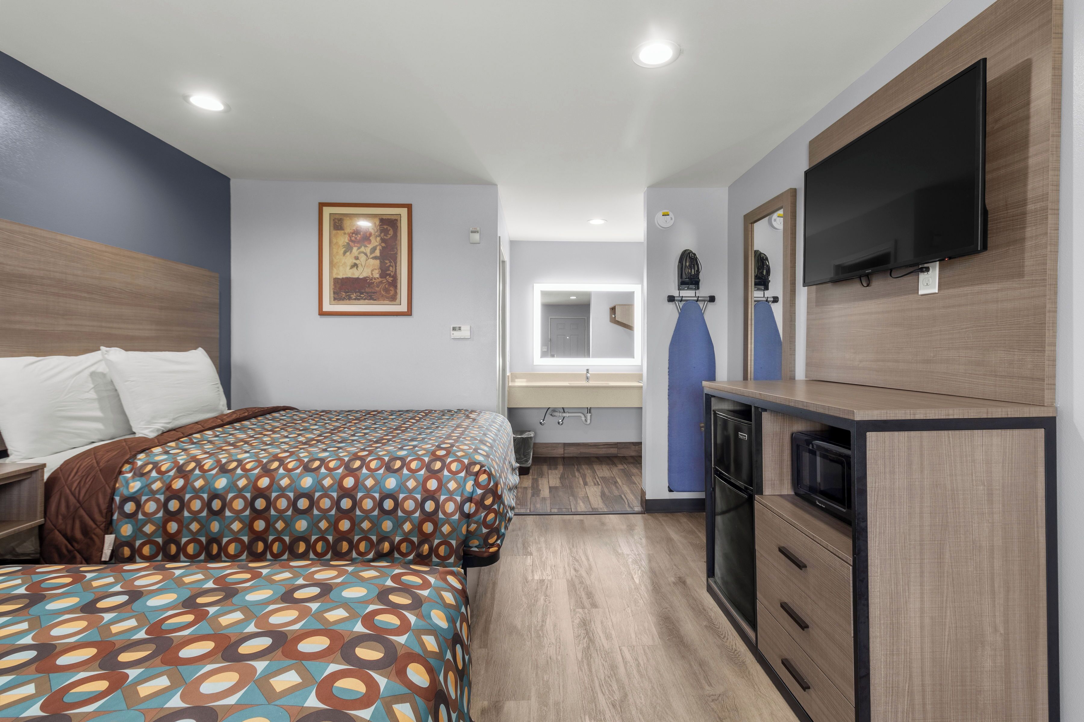 A modern hotel room with two beds, a flat-screen TV, a microwave, and a small kitchenette.