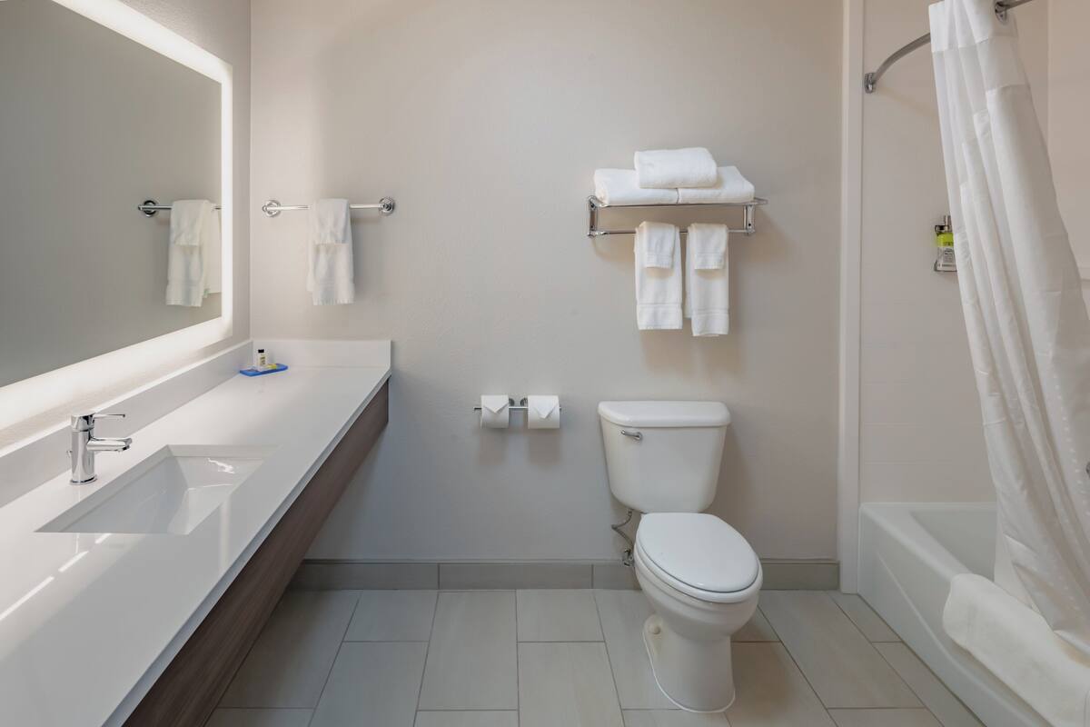 A modern bathroom with a large mirror, a sink, a toilet, and a shower area.