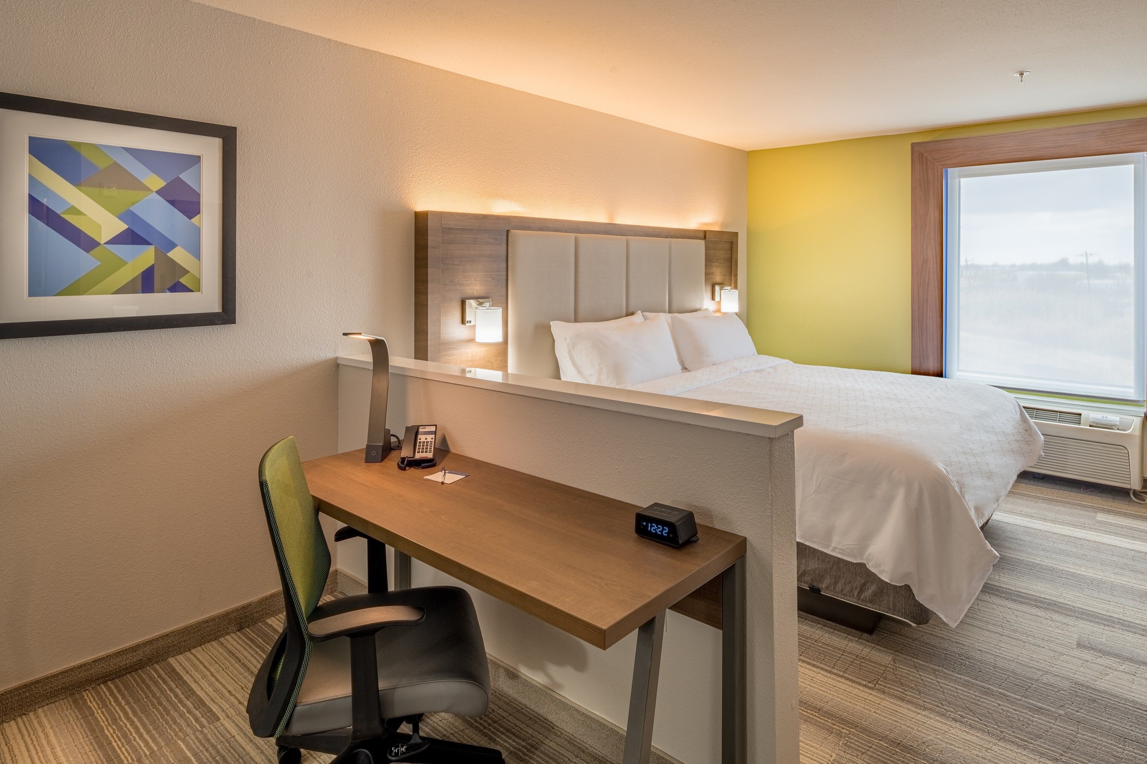 Una habitación de hotel con una cama, un escritorio con una silla, un teléfono y un reloj.