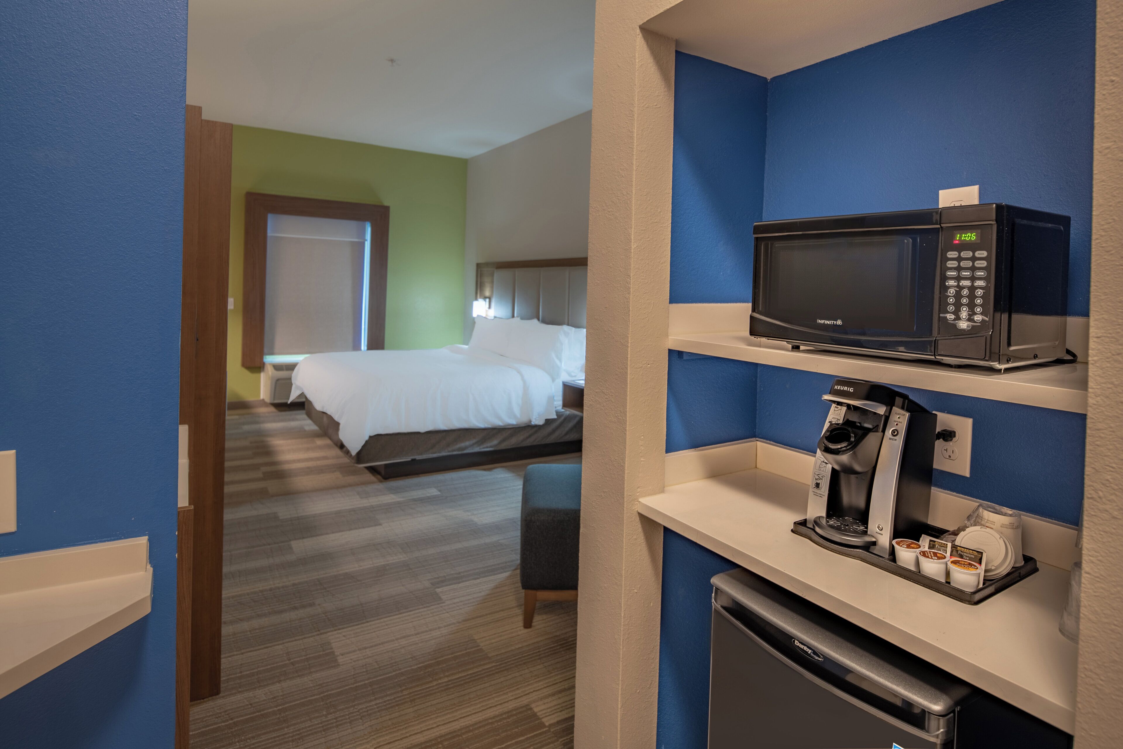 A hotel room with a bed, a microwave, a coffee machine, and a small refrigerator.