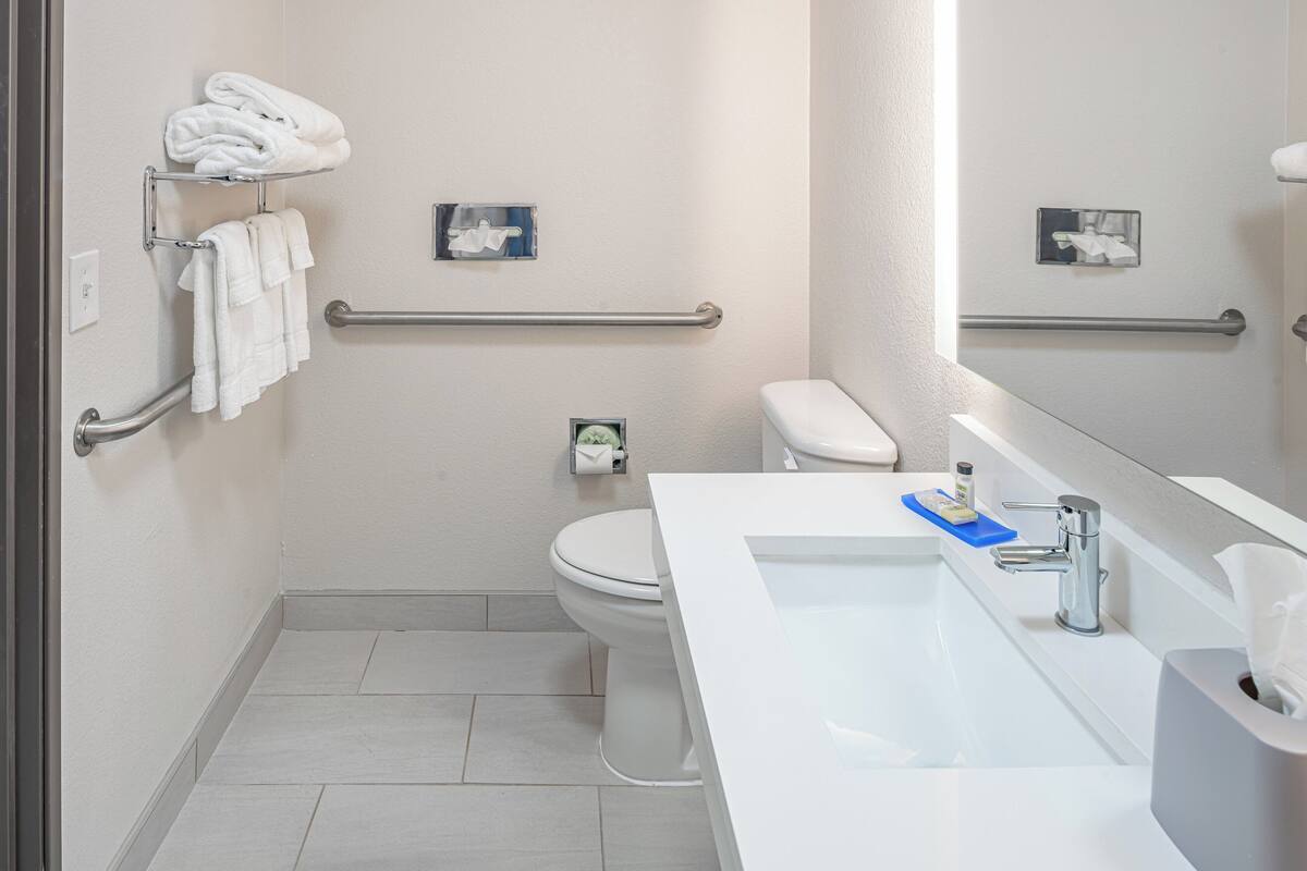 A modern bathroom with a white sink, a toilet, and a handrail.
