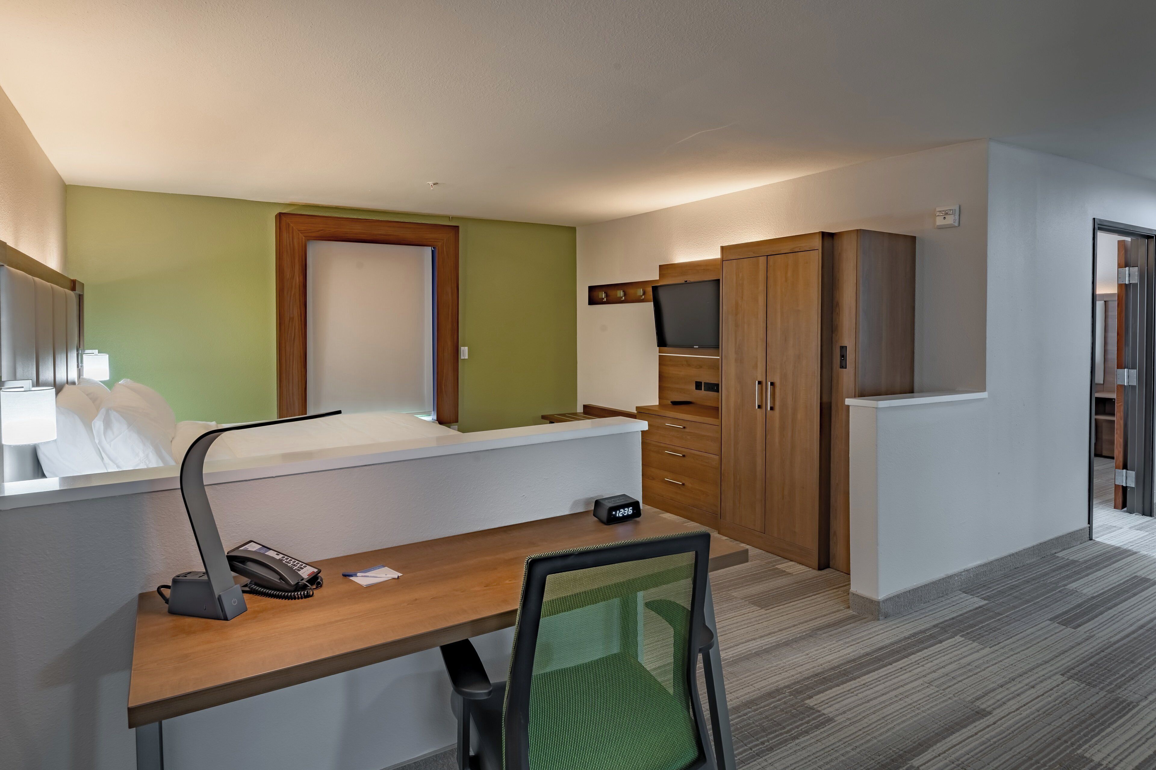 A hotel room with a bed, desk, chair, and a TV mounted on the wall.