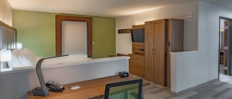 Habitación de hotel con cama, escritorio, silla y televisor montado en la pared.