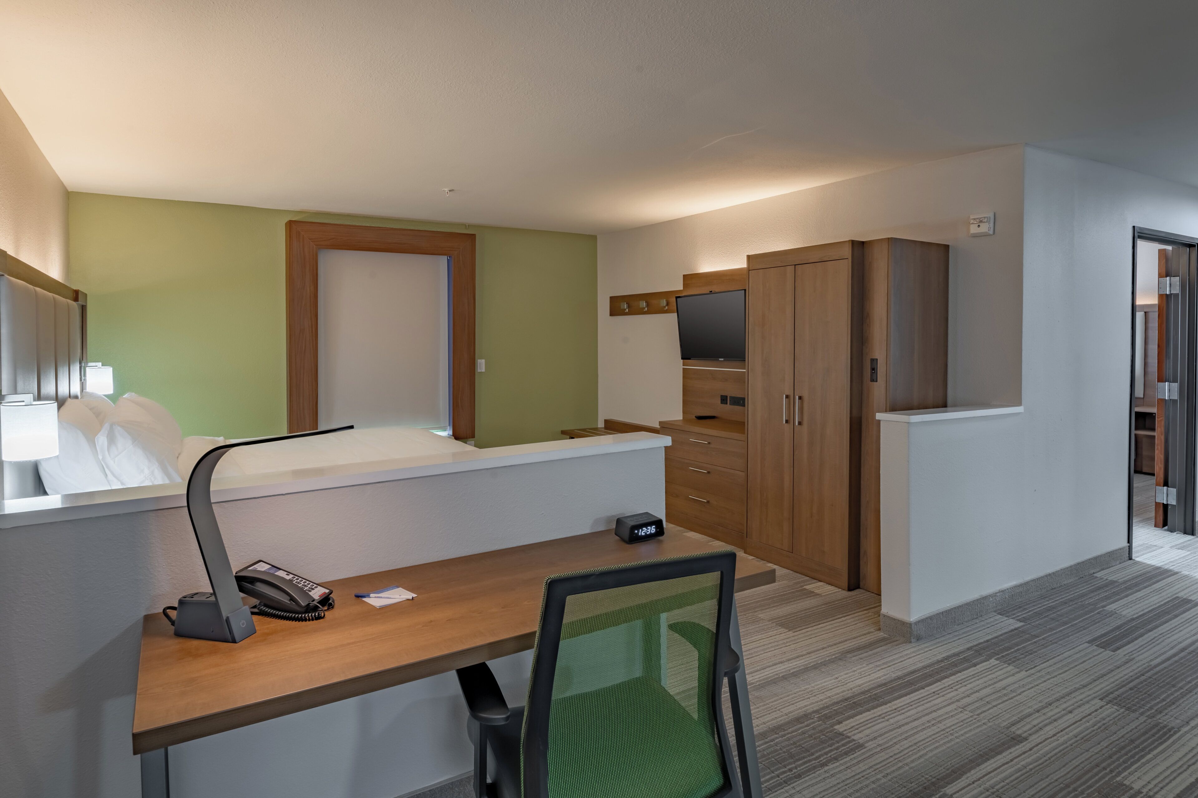 Una habitación de hotel con escritorio, silla, cama, televisor y armarios.