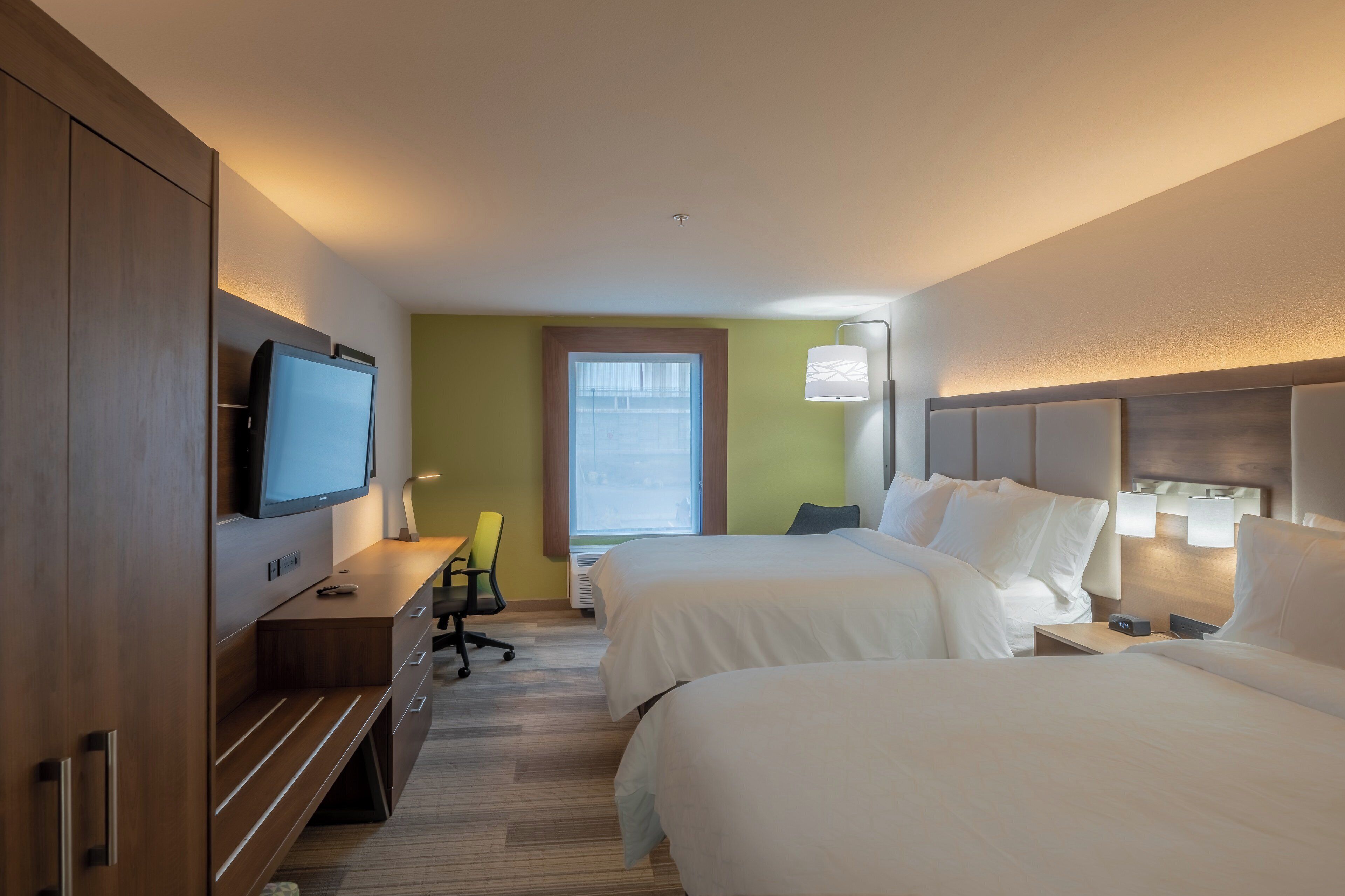 Una habitación de hotel con dos camas, un escritorio, un televisor y una ventana.