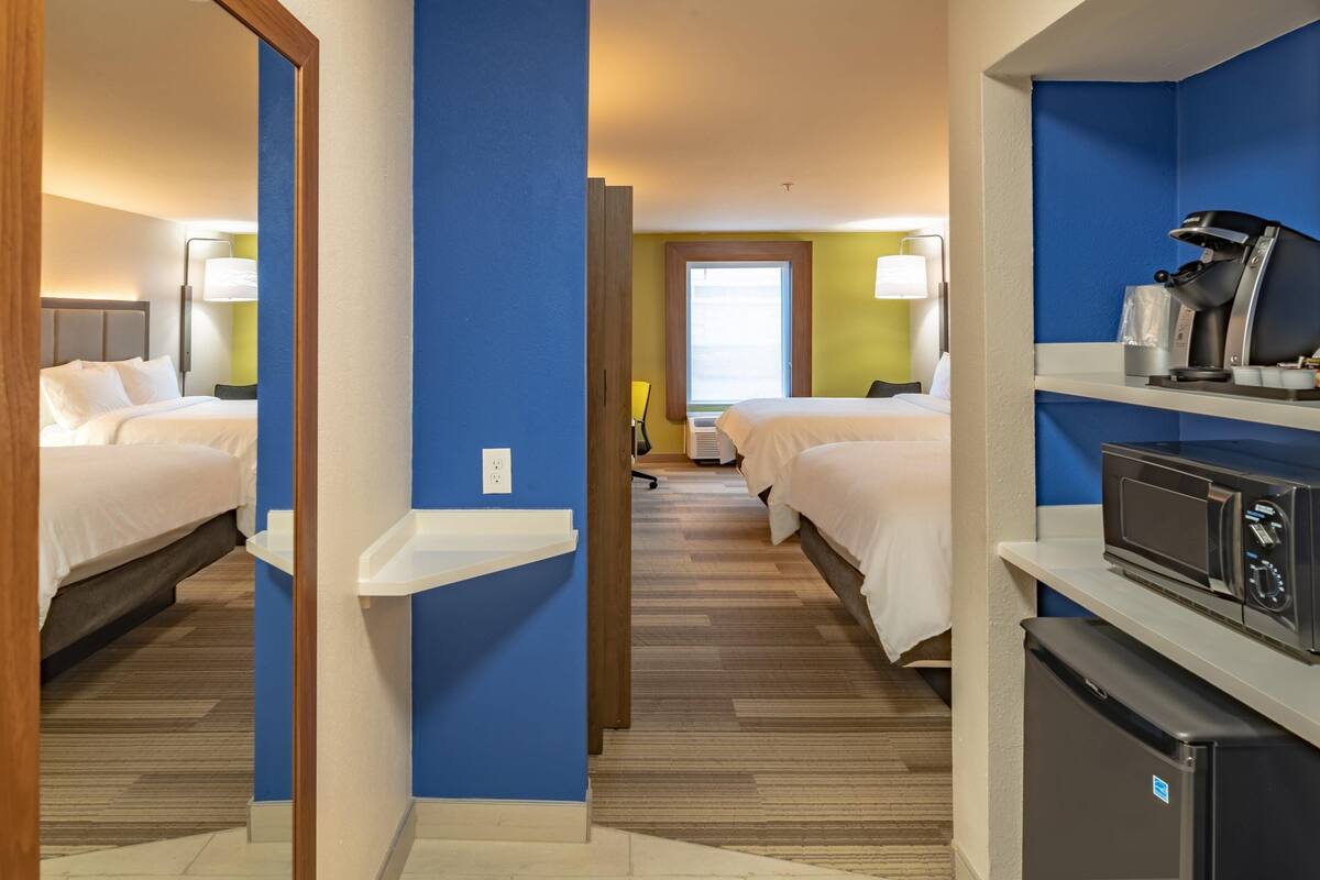 A hotel room with two beds, a kitchenette, and a bathroom with a window.