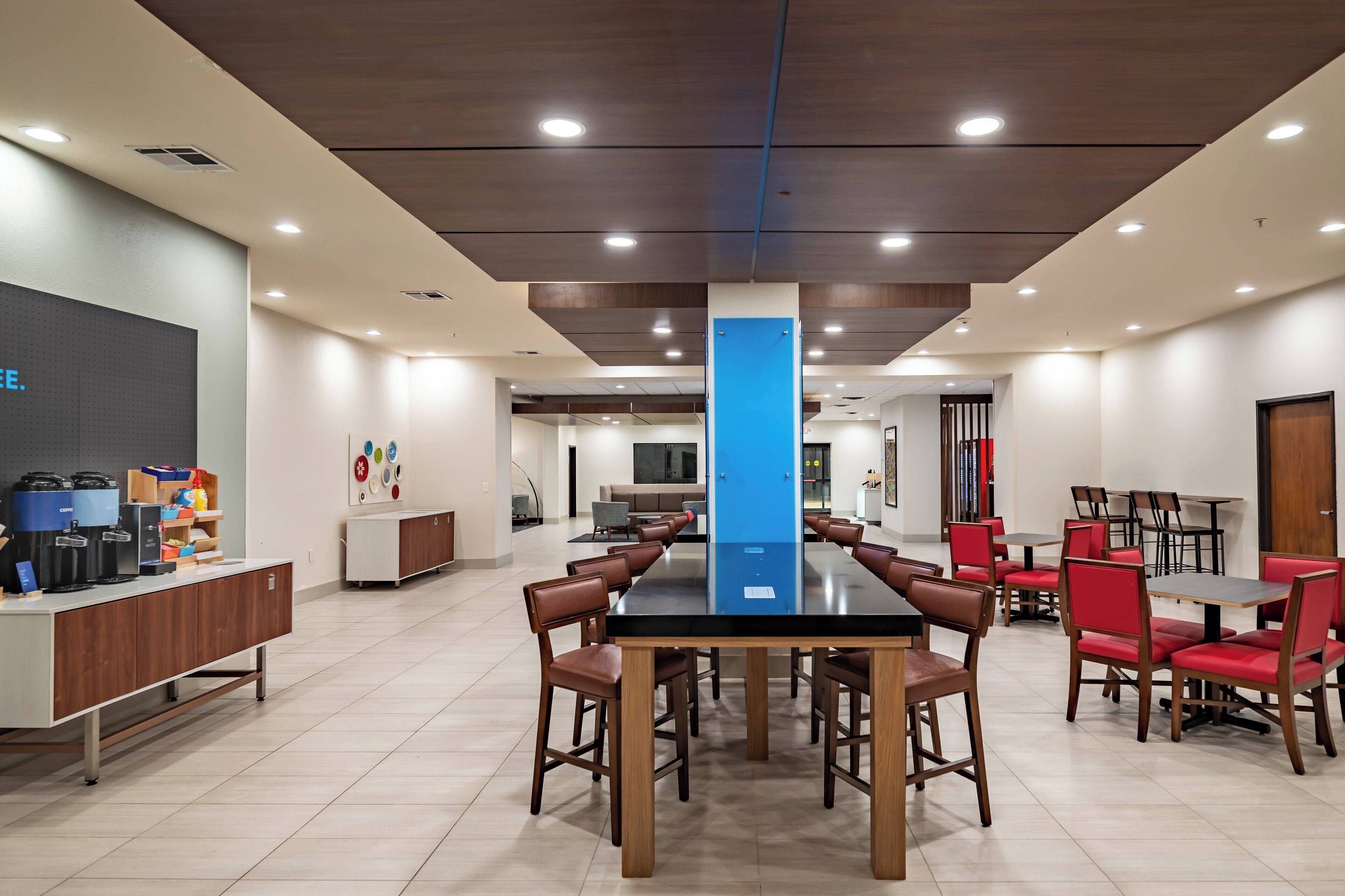 A modern conference room with a long table, red chairs, and a coffee station.
